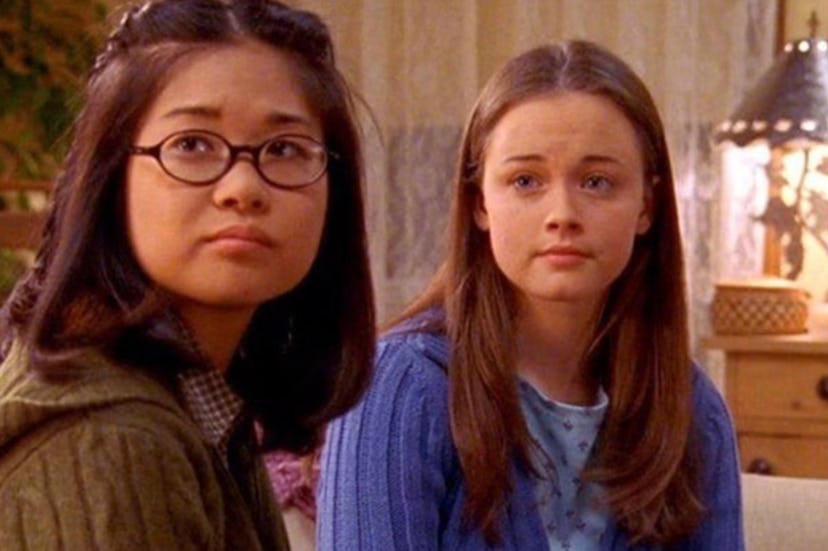 Two young girls, one with glasses and a green jacket, the other in a blue sweater, looking slightly ...