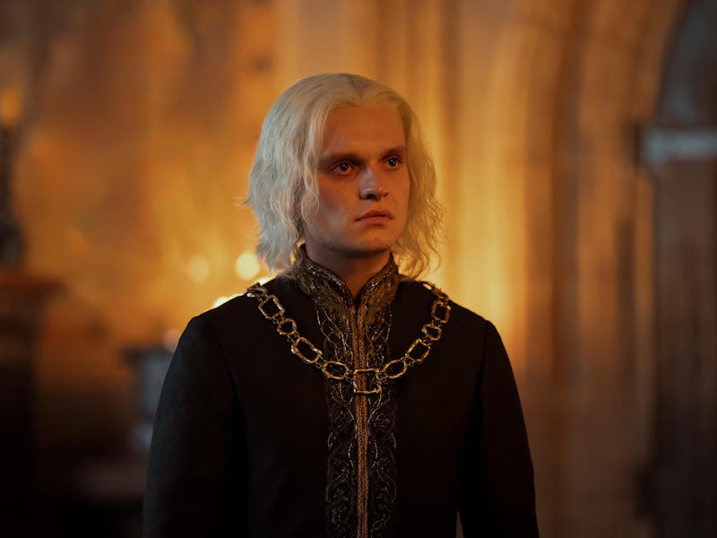 A man with long white hair and intense expression, wearing medieval-style armor, stands in a dimly l...