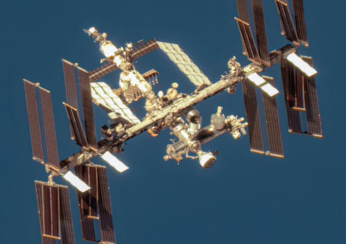 International Space Station in orbit with solar panels extended, set against the deep blue of Earth's atmosphere.