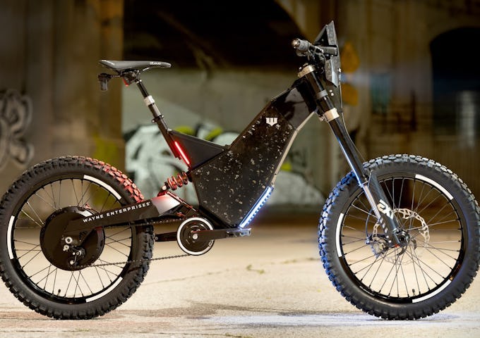 Electric mountain bike with studded tires and blue neon lights parked in an industrial setting.