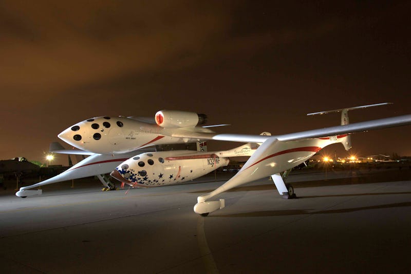 SpaceShipTwo and White Knight Two on a runway at night, illuminated under a dusk sky.