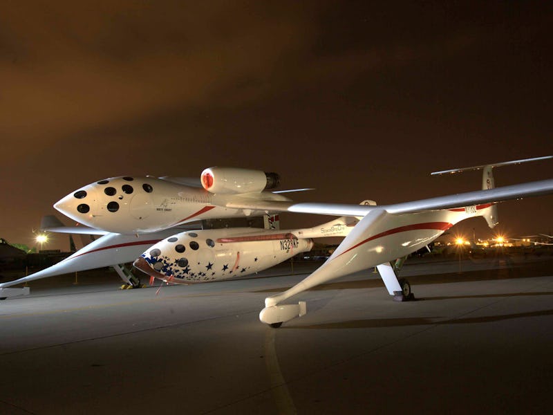 SpaceShipTwo and White Knight Two on a runway at night, illuminated under a dusk sky.