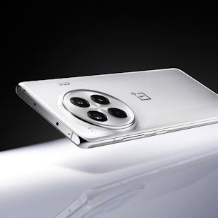 A white OnePlus smartphone with a triple camera setup on a reflective surface, partially illuminated by a soft light.