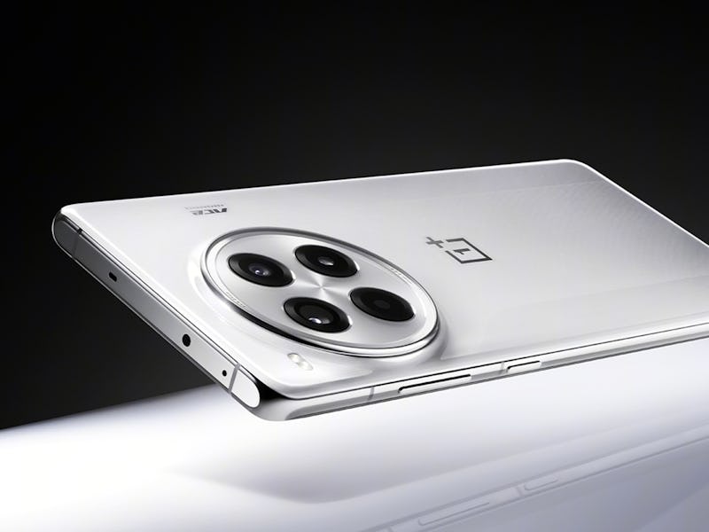 A white OnePlus smartphone with a triple camera setup on a reflective surface, partially illuminated...