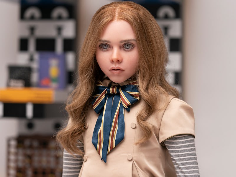 Young woman with long, wavy blonde hair in a beige dress and striped scarf, standing in a room with ...