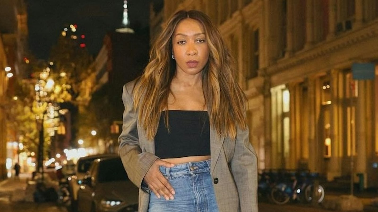 Karen Blanchard poses on a Soho sidewalk at night wearing an oversize blazer, cropped tube top, wide leg jeans, and black boots.