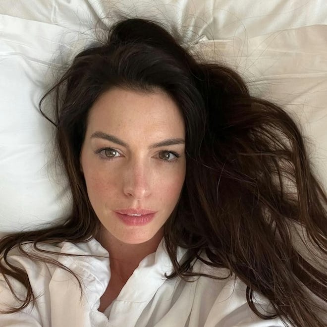 Anne Hathaway selfie with white robe on laying against white pillows