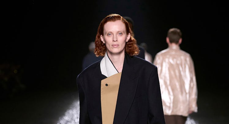 Model in oversized black blazer and beige dress walking on metallic confetti runway.