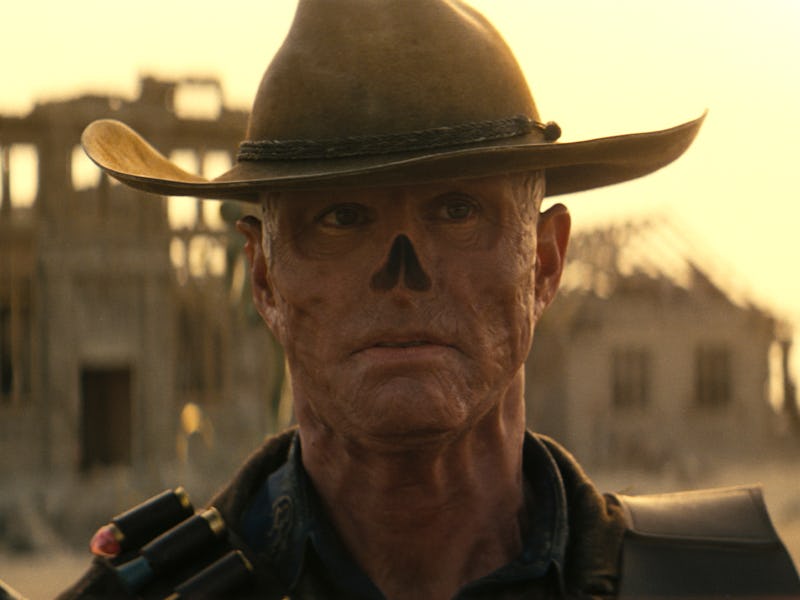 Close-up of a man in a cowboy hat with war paint on his face, against a desert landscape with dilapi...