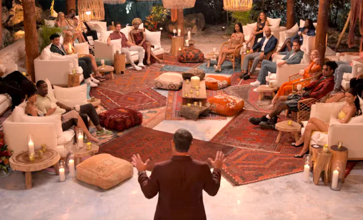 A diverse group of people seated in a cozy, candle-lit room with rustic decor listening attentively ...