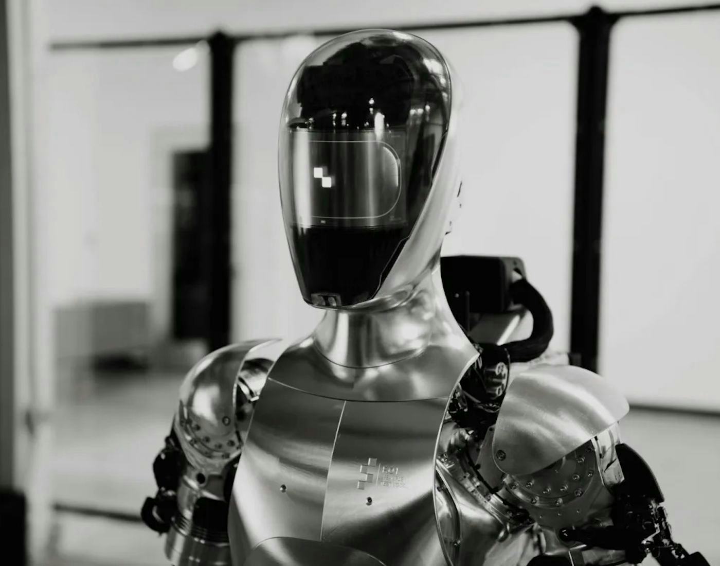 A humanoid robot with a reflective head and torso made of sleek, metallic material, standing in an indoor setting.