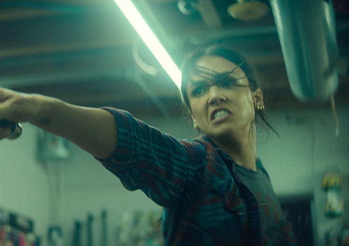 A determined young woman in a plaid shirt throwing a punch in a dimly lit workshop.
