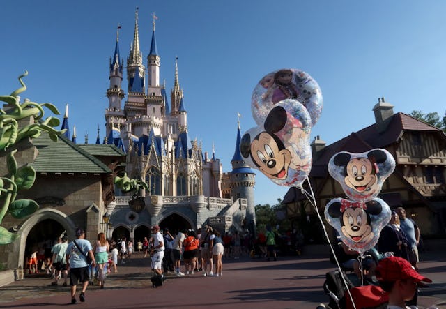 Cinderella Castle at Magic Kingdom with visitors walking and Mickey Mouse balloons attached to a str...