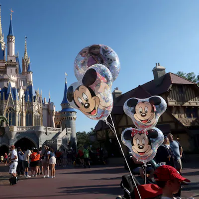 Cinderella Castle at Magic Kingdom with visitors walking and Mickey Mouse balloons attached to a stroller in the foreground.