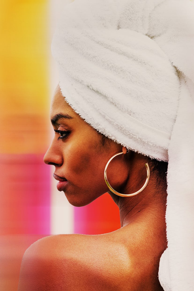 Profile of a woman with a towel wrapped around her head and a large hoop earring, against a colorful...