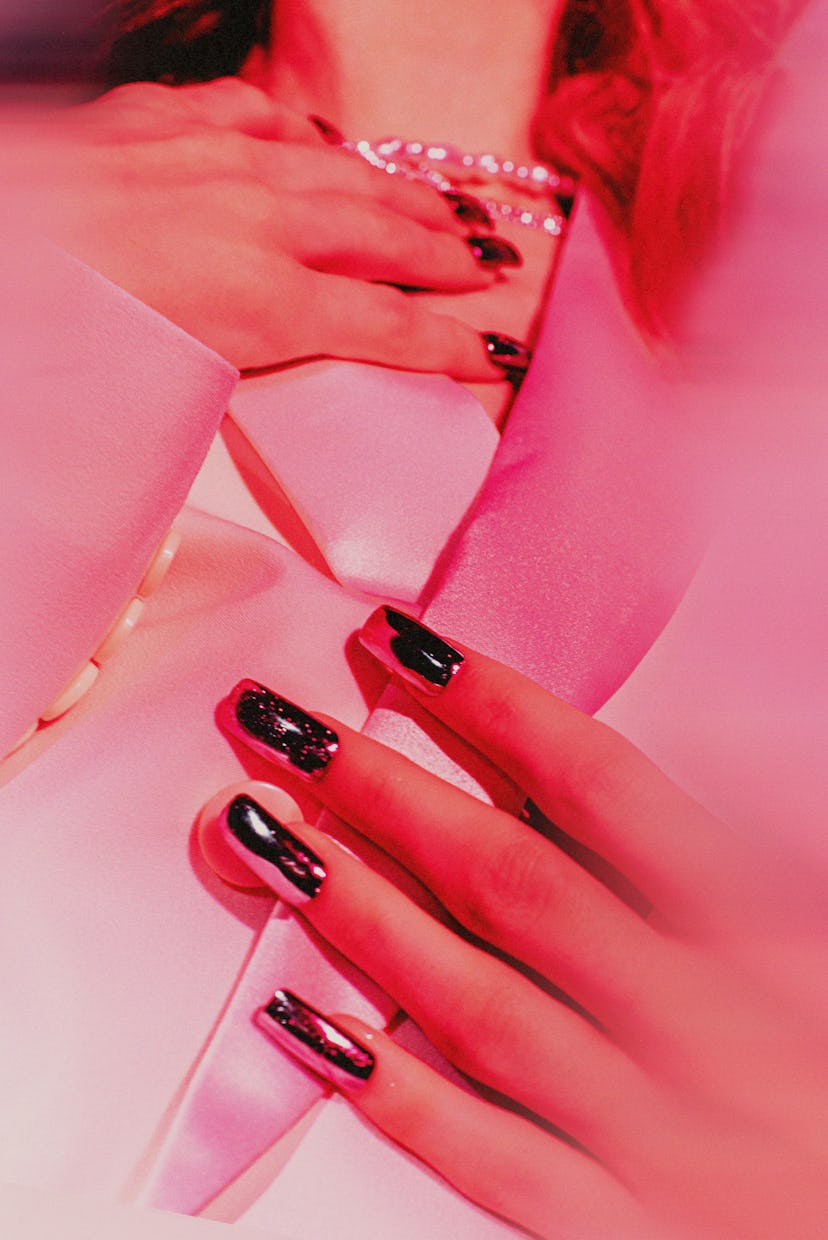 Elegant hands with black gemstone nail polish adjusting a pearl necklace, against a pink satin shirt...