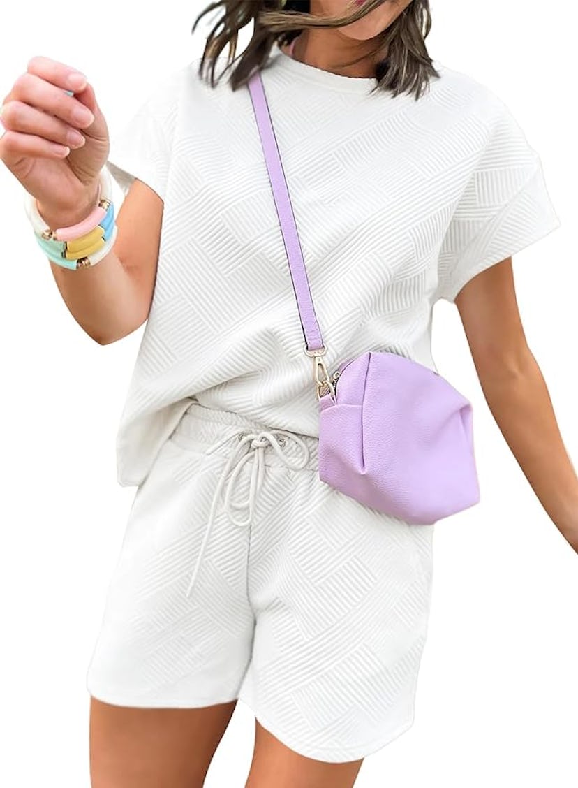 Woman in white patterned outfit with a purple crossbody bag and colorful bracelets, walking in a non...