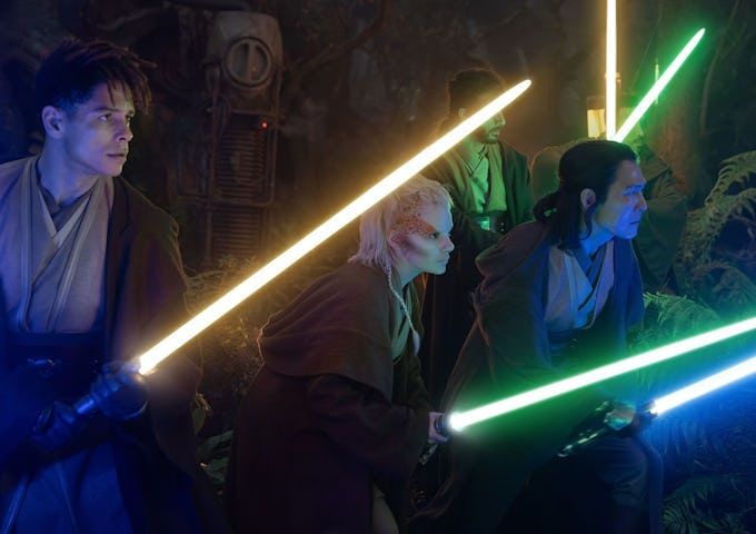 Three characters holding lightsabers, two green and one blue, standing alert in a dimly lit, mysterious setting.