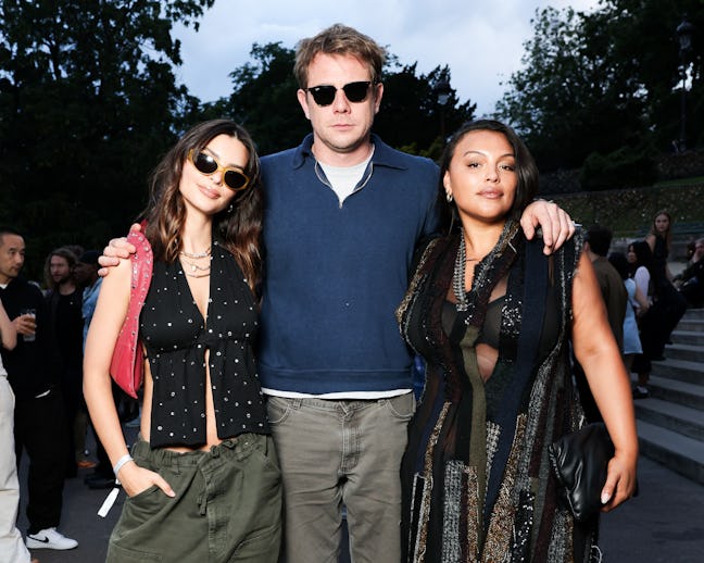 Three people posing together outdoors, two women and one man in sunglasses, casually dressed at a so...