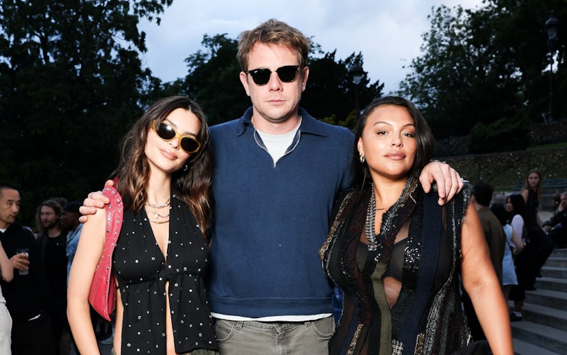 Three people posing together outdoors, two women and one man in sunglasses, casually dressed at a so...