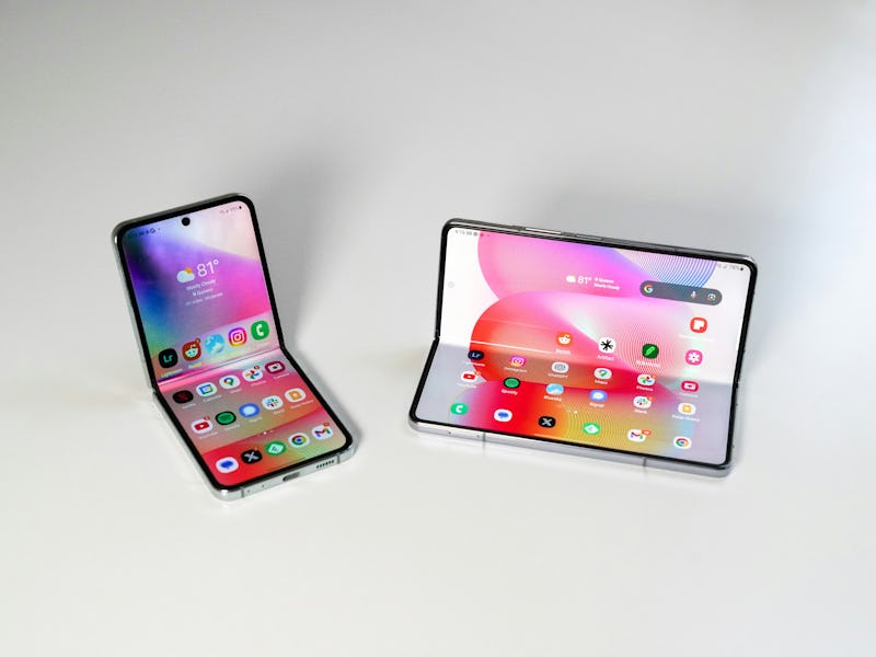 Two modern foldable smartphones in an open position, displayed on a clean white surface. One is upri...