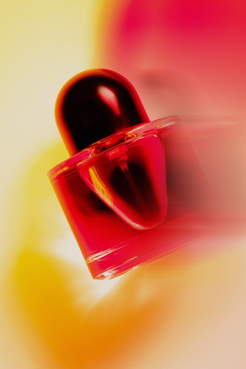 A glossy, red perfume bottle with a dramatic black cap, captured in motion against a blurred yellow ...