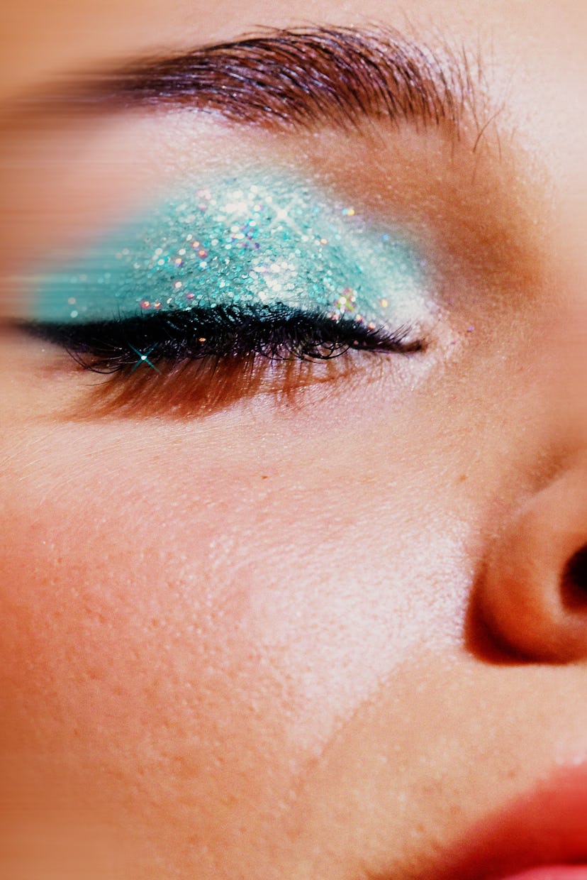 Close-up of a person's eye with vibrant turquoise glitter eyeshadow and black mascara, highlighting ...