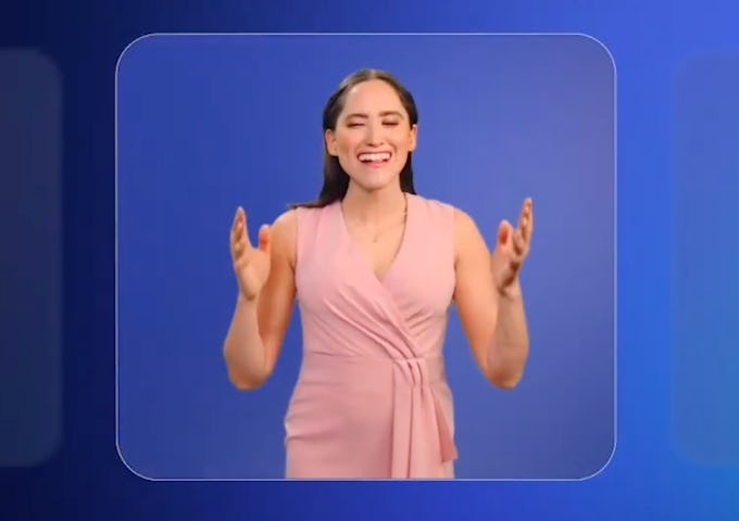 A woman in a pink dress clapping and smiling against a bright blue background.