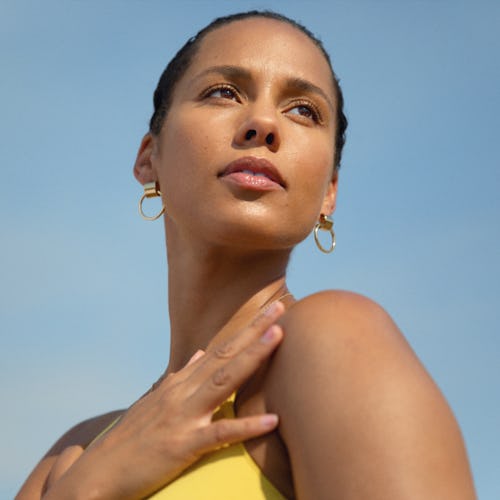 Portrait of a Alicia Keys with her head held high, wearing hoop earrings and a yellow top, against a…