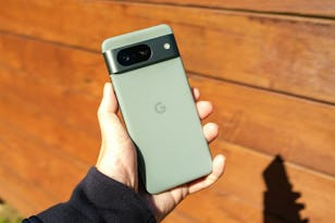 A hand holding a Google smartphone with a distinctive camera bar, against a wooden background.