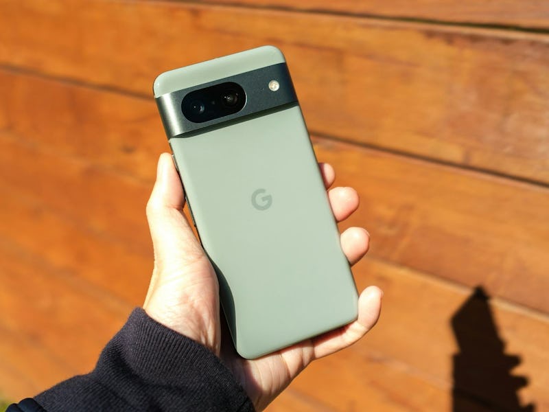 A hand holding a Google smartphone with a distinctive camera bar, against a wooden background.