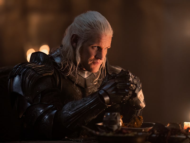 A knight with long white hair, wearing dark armor, sits at a dimly lit table intently gazing while h...