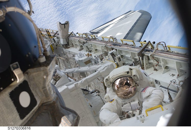 An astronaut wears a spacewalk suit, as he stands inside the open cargo bay of the airplane-shaped S...
