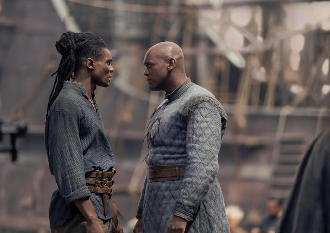 Two men in historical costumes face each other intently against a backdrop of a dimly lit shipyard, portraying a tense moment.