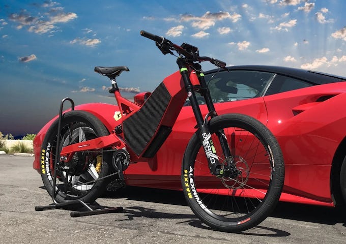 Electric bike propped against a red sports car under a blue sky with clouds.