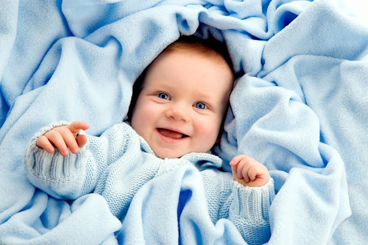 A joyful baby in a blue sweater wrapped in a soft blue blanket, smiling happily.