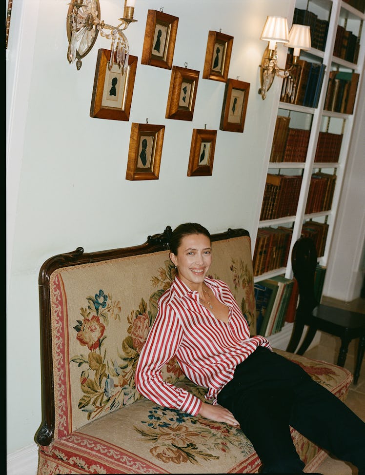 Woman in a red and white striped shirt reclining on an antique sofa, surrounded by framed portraits ...