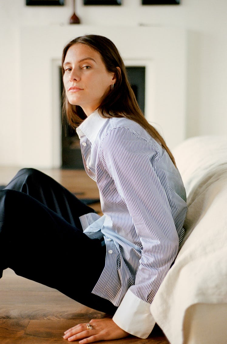 A woman in a striped shirt sits on the floor, looking back over her shoulder in a bright, stylish ro...