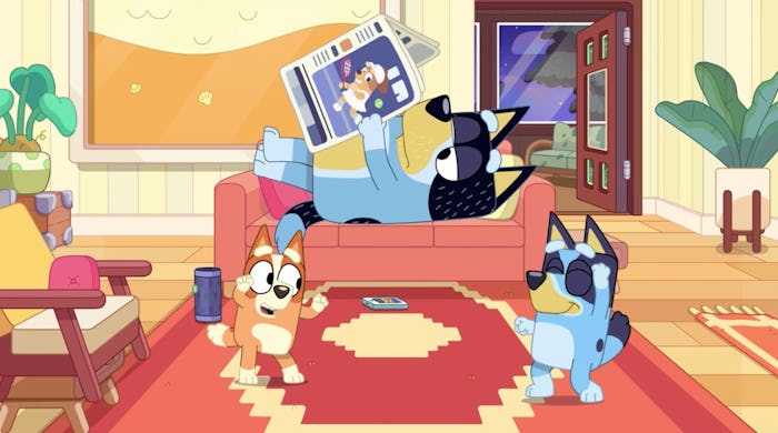 Bingo and Bluey dance in the living room while Bandit reads a newspaper on the couch.