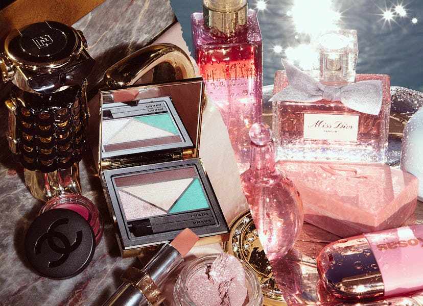 Assorted luxury cosmetic products including makeup and perfumes, displayed on a glossy surface with ...