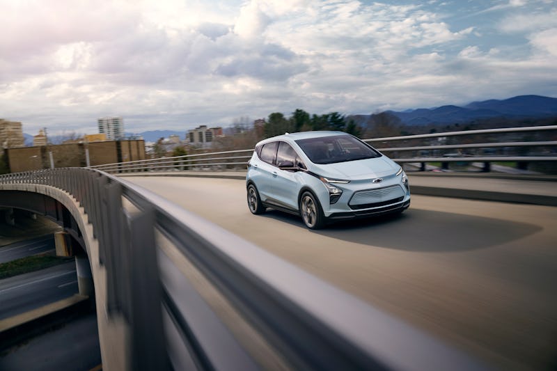 Silver electric SUV driving on a curvy overpass, with blurred city and mountain background, capturin...