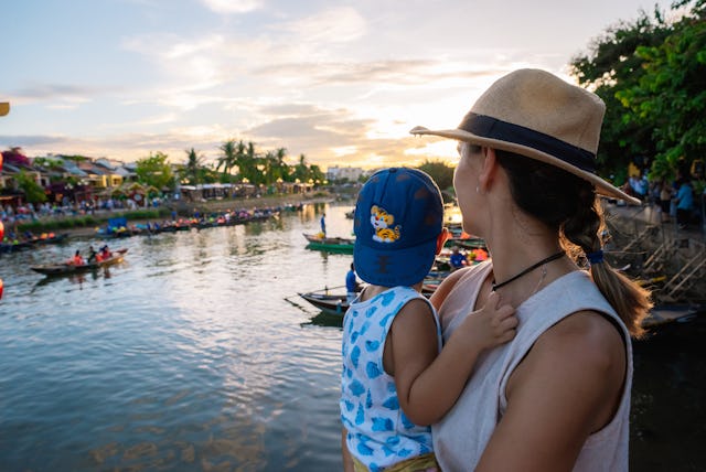 Young woman holding her child in her arms while admiring the Thu Bon river at sunset.