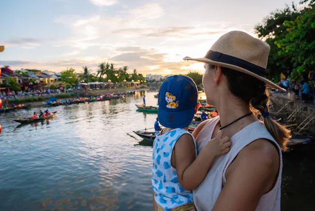 Young woman holding her child in her arms while admiring the Thu Bon river at sunset.