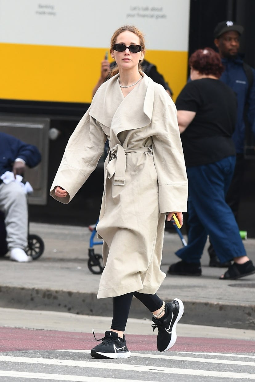 Jennifer Lawrence wears a trench coat with leggings and sneakers. 