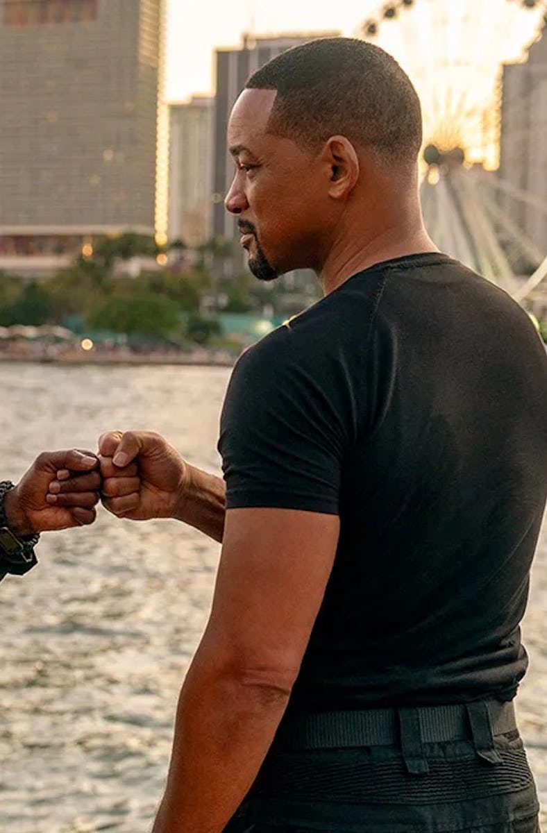 Two men fist-bumping on a waterfront with a cityscape behind them during sunset. They are engaged in...