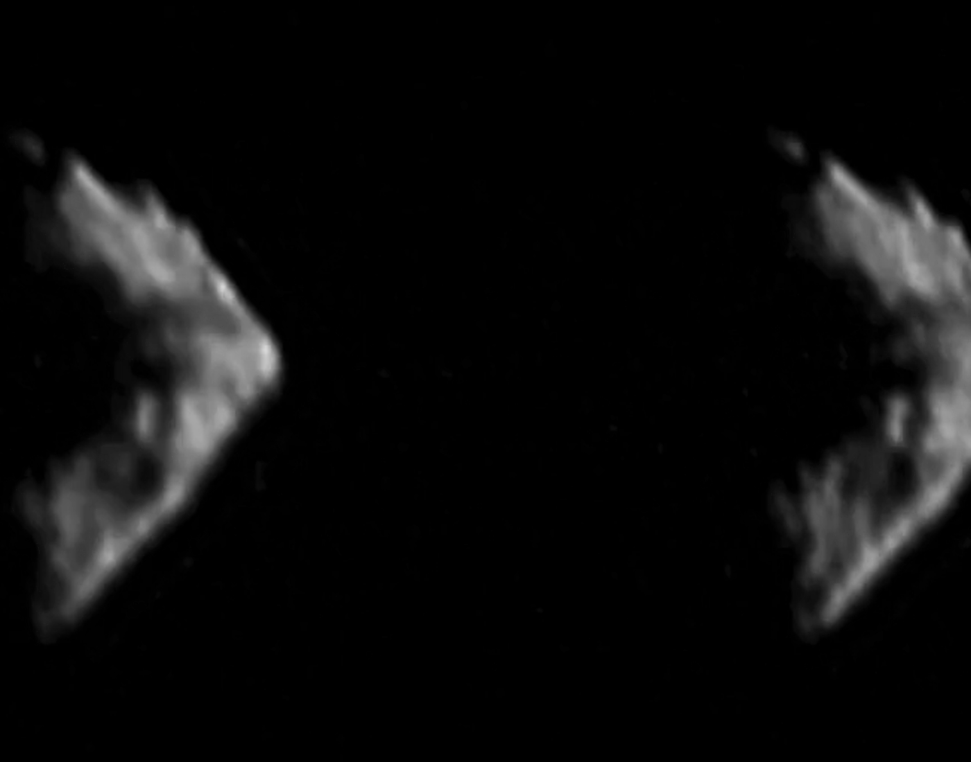 Blurred image of two irregular, angular shapes against a dark background, suggesting a low-resolution, close-up view of celestial objects or debris.
