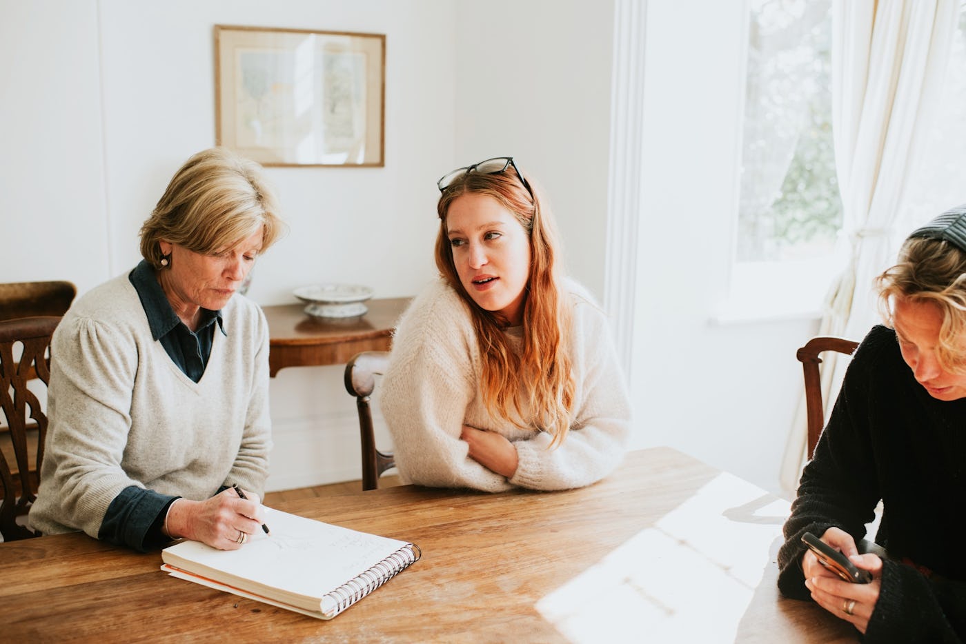 An adult woman sits at a dining table with her mom, who takes notes on a notepad.