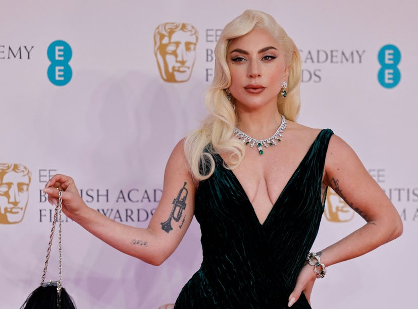 Woman in a black gown with a deep neckline and tattoo on arm posing at a film award event.