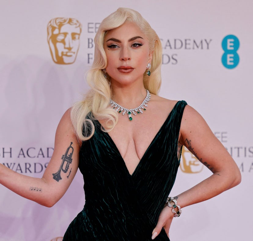 Woman in a black gown with a deep neckline and tattoo on arm posing at a film award event.