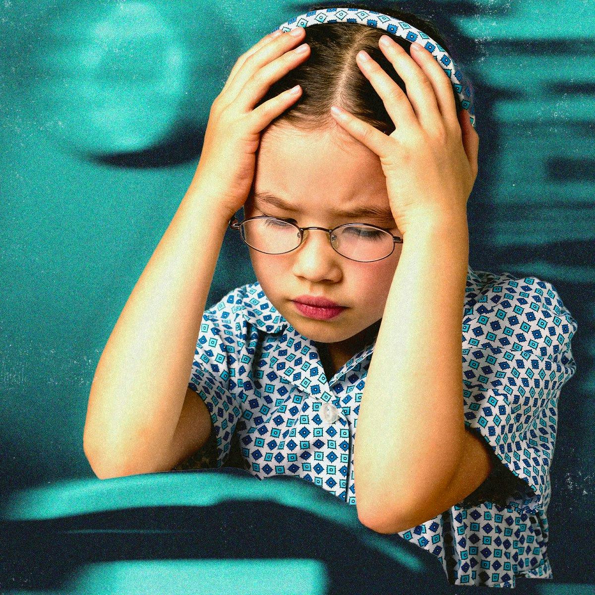 Young girl with glasses looking distressed, holding her head in her hands, against a teal background.